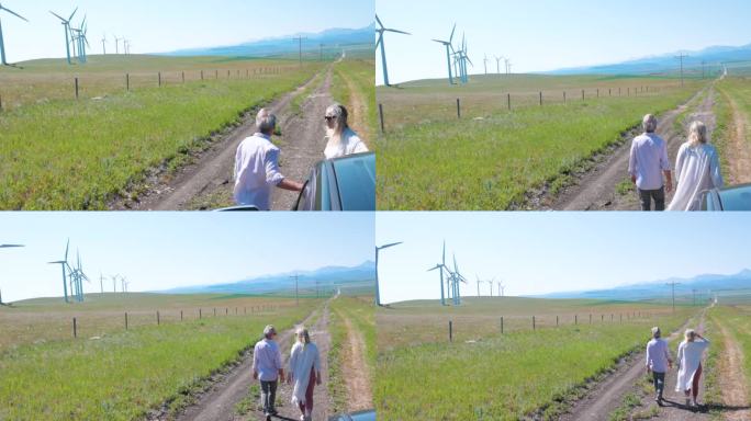一对老年夫妇走在风力涡轮机下面的小路上