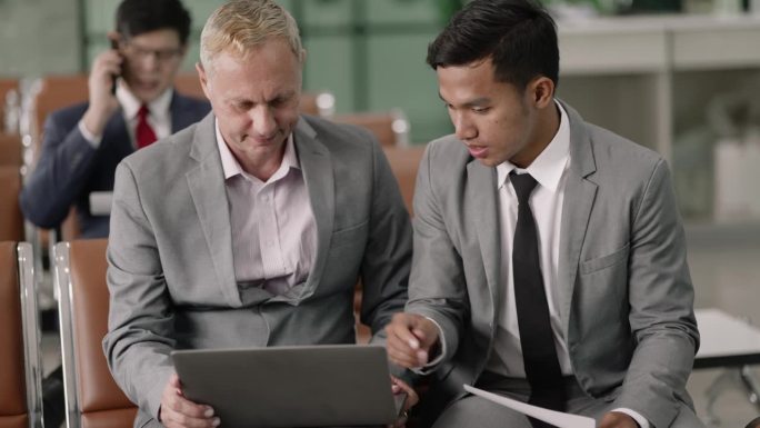 不同的商人和男同事在机场候机楼门口用笔记本电脑讨论信息。