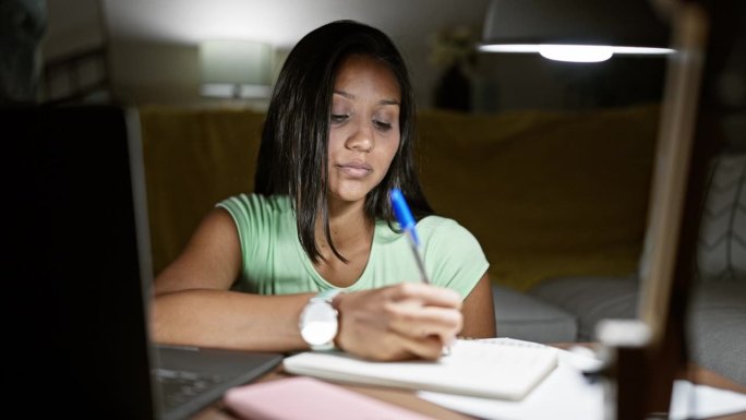 年轻的拉丁女人在家里用笔记本电脑记笔记看手表
