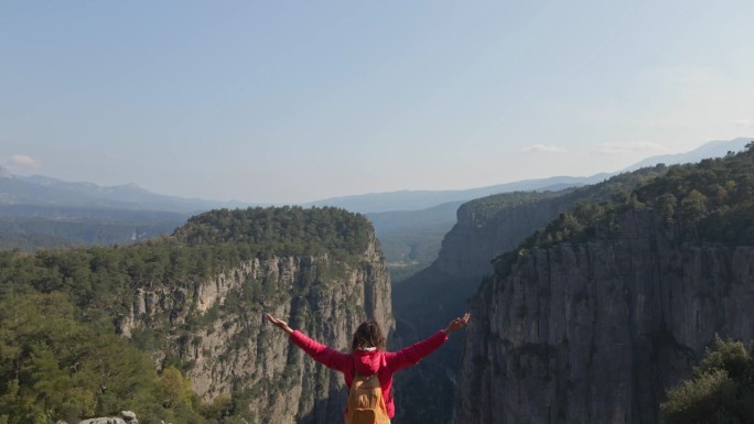 泰兹峡谷的鸟瞰图。女孩站在山上欣赏美丽的景色。在峡谷背景下的悬崖上，穿着红色夹克的女游客徒步旅行。神