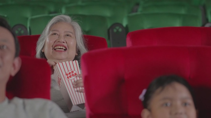 幸福的家庭在电影院享受爆米花和看一部有趣的电影。不同种族的人都喜欢在电影院看电影。团体游憩活动和娱乐