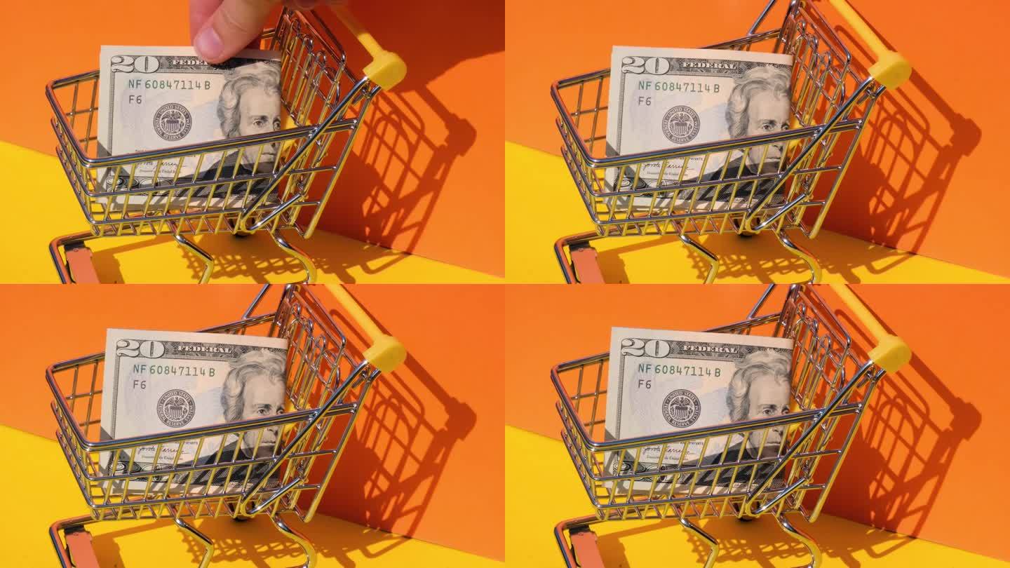 手加20美元钞票在玩具超市购物车黄色背景的钱。销售一篮子美元钞票。最低生活工资概念:贷款、投资养老、