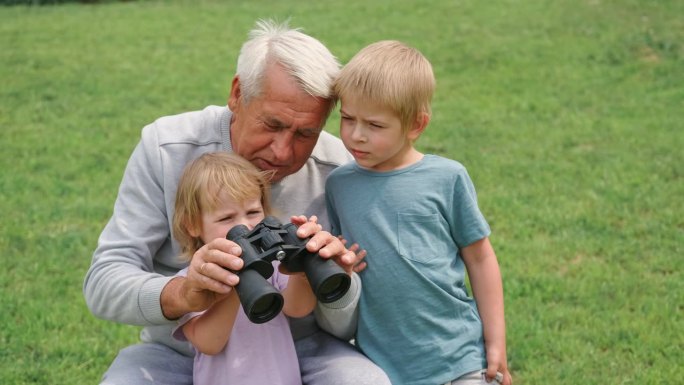 爷爷和孙子在公园里用望远镜。快乐的家庭时光。老人爷爷和孩子们玩男孩和女孩。夏天的一天。微笑的老男人和
