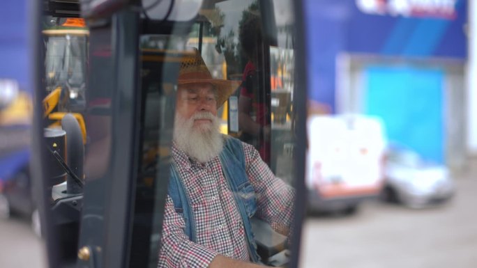 后视镜里，一个戴草帽的白人老头坐在拖拉机车厢里。自信的农民选择收割机在户外购买新车。