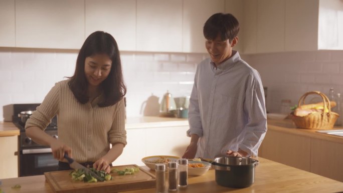 一对韩国年轻夫妇在家做饭的照片。相爱的男女朋友在厨房准备晚餐，一边做美味的食物一边进行有趣的交谈
