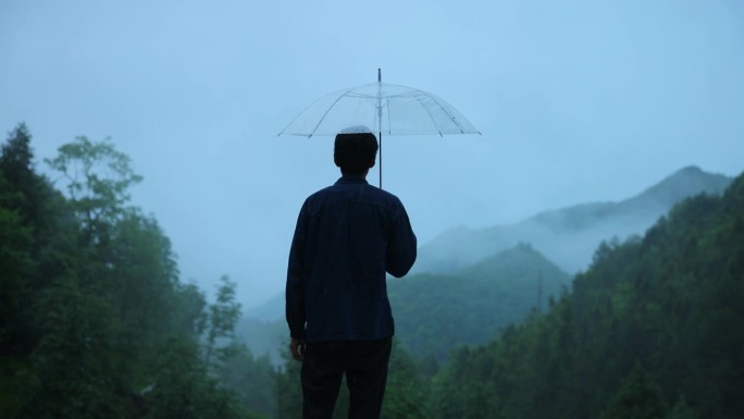 男人在雨天打着透明的伞看山