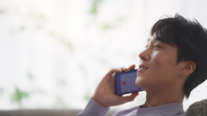 一个韩国年轻人坐在舒适的沙发上，用智能手机进行了一次有意义的电话交谈，深入讨论了个人成长和生活目标