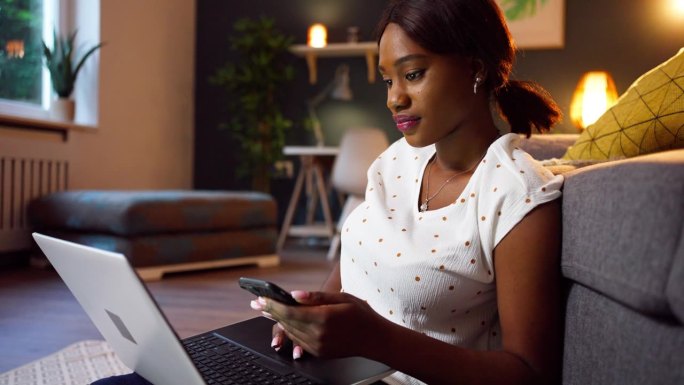 年轻的黑人女性一边用笔记本电脑工作，一边用手机