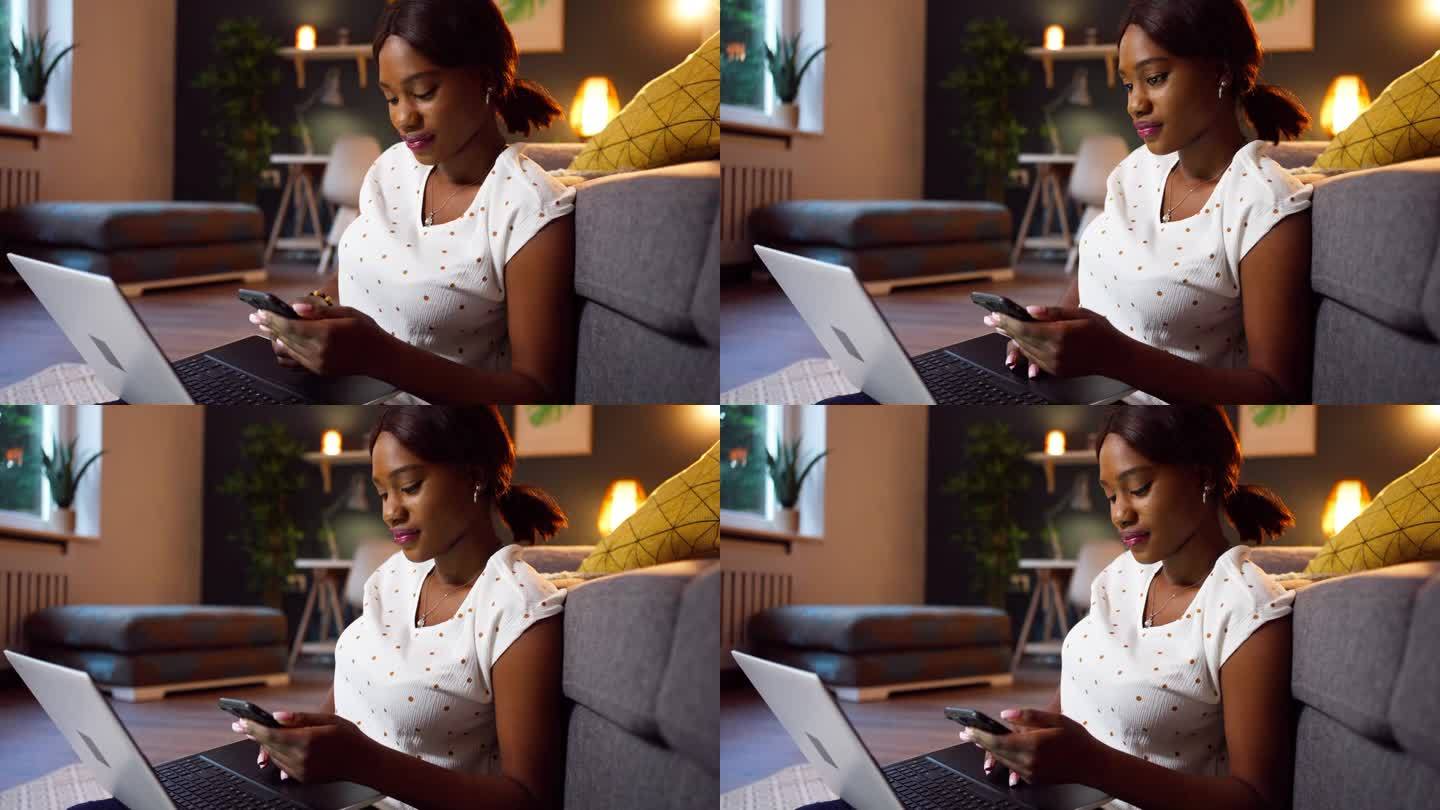 年轻的黑人女性一边用笔记本电脑工作，一边用手机