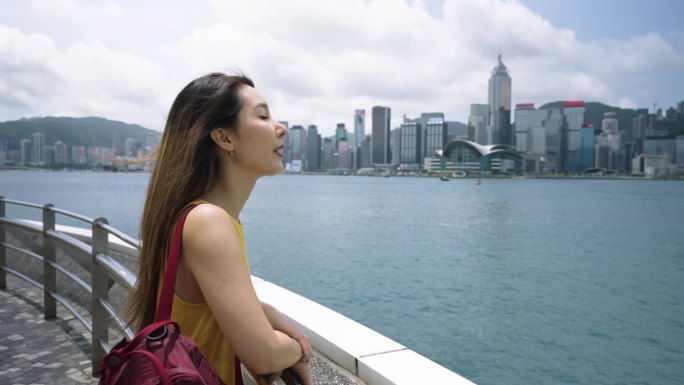 亚洲年轻女子在维多利亚港观光，眺望香港城市