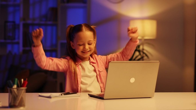 一个可爱的小女孩坐在客厅的桌子旁使用笔记本电脑。孩子示范性地按下按钮，对结果非常满意，像敲鼓一样敲打