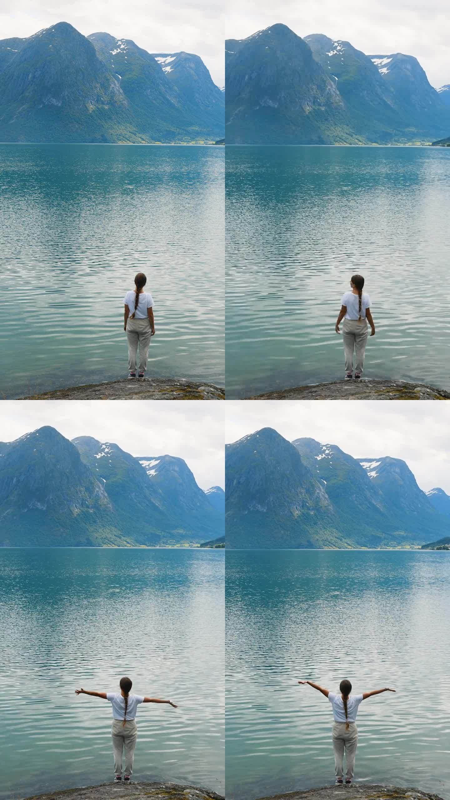 在挪威，一名女子高举双臂，眺望湛蓝的湖泊和山脉