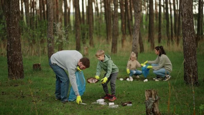 孩子和家长在森林里捡垃圾，保持游乐区清洁，保护生态