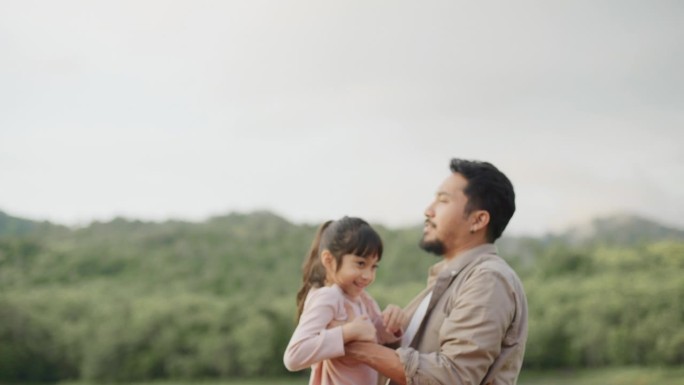 度假时，一位亚洲父亲抱着他的小女儿在草地上露营。
