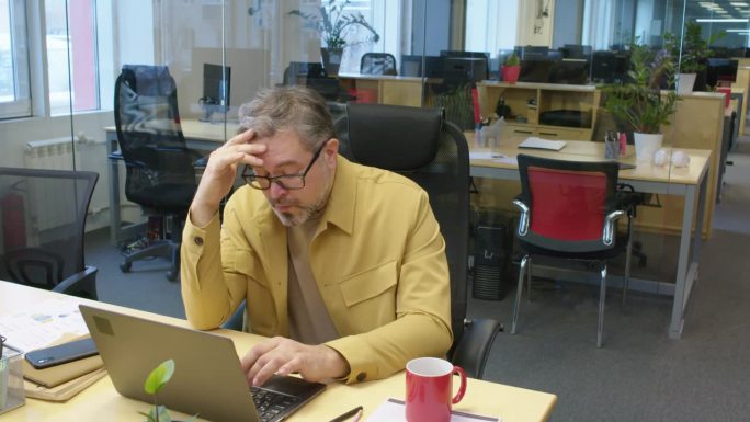 疲惫的男经理在办公室用笔记本电脑工作