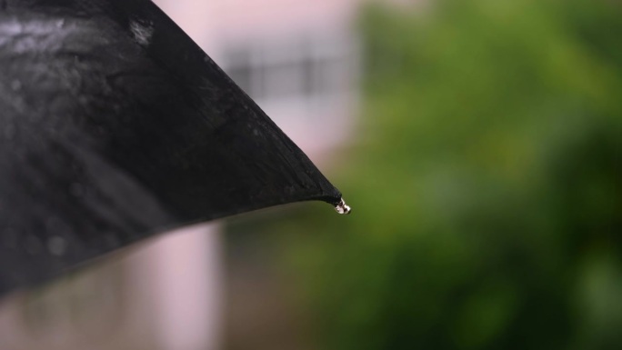 雨淋在城市里散步。雨滴落在黑色的伞上，从伞上流下来。特写镜头。
