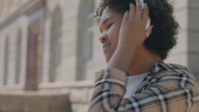 欢快的非洲裔美国女孩在城市街道外用耳机和智能手机听音乐跳舞的慢动作