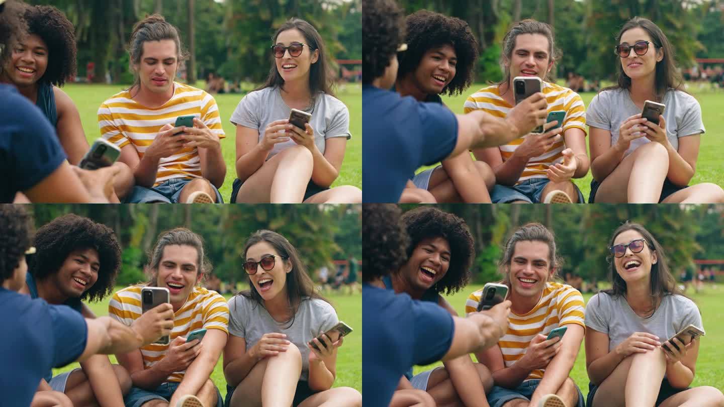 一群多民族青年朋友坐在公园里有说有笑。形形色色的朋友在智能手机上看搞笑视频