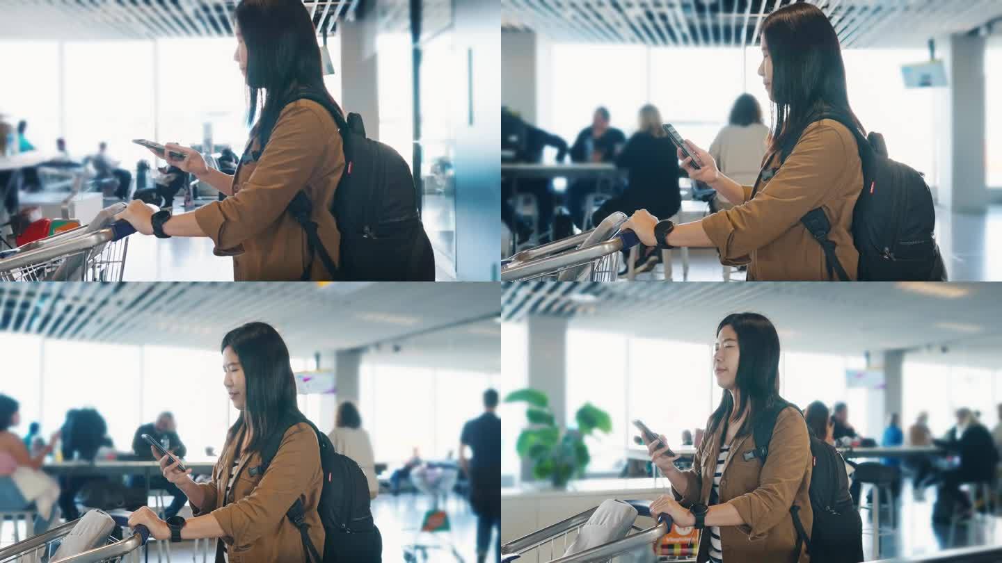 在机场门口的走道上，亚洲女旅客边走边用手提行李车用手机