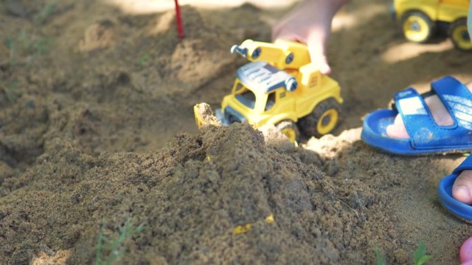 一个亚洲男孩用玩具挖掘机和自卸卡车玩和挖沙子。