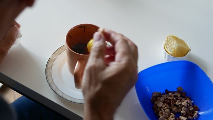 厨房桌上一杯热茶，一位老人喝着柠檬茶。香气扑鼻的茶，一位老人的手端着一杯茶。