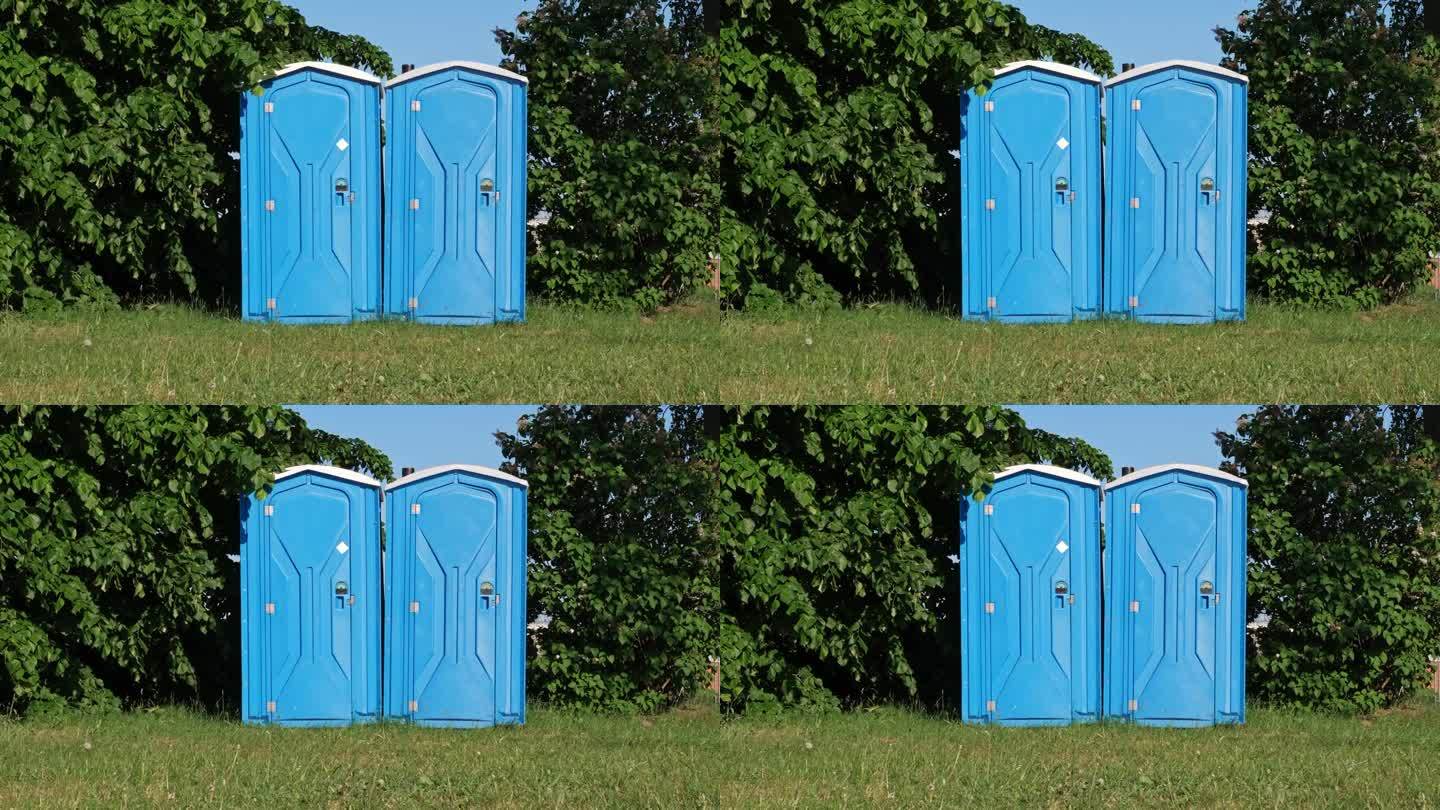 在露天音乐节期间，一对蓝色塑料移动公共厕所站在高高的草地中间
