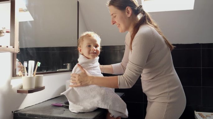 年轻有爱心的母亲在洗澡后用浴巾给儿子梳头。育儿理念，幸福与儿童卫生