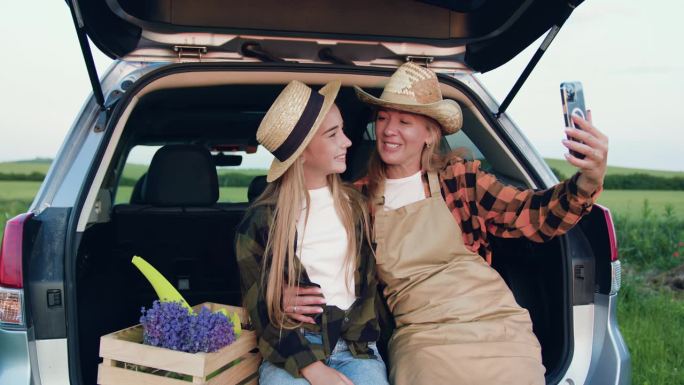 农民一家，母亲和女儿穿着围裙和帽子，坐在汽车后备箱里，旁边是一个装有新鲜薰衣草的木箱，在日落时分用手