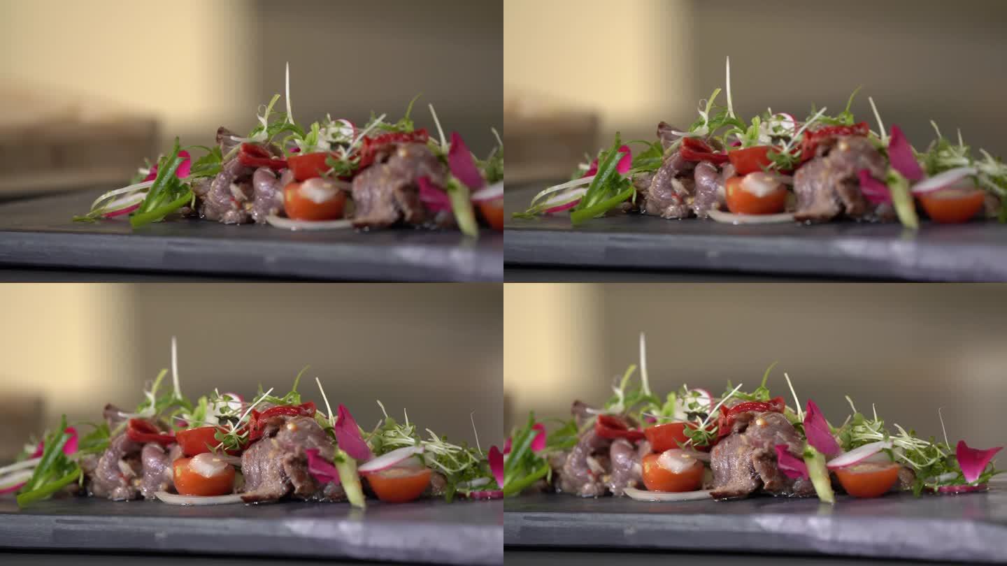 辣味泰式牛肉切片沙拉是用多种食材制作的，包括绿色蔬菜、红萝卜和粉红色的花。在长方形石板上，排列整齐。