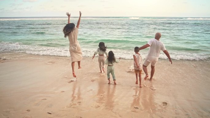 一个快乐的家庭，男人和女人带着孩子在海洋海滩的海水中奔跑。热带旅游可爱的孩子们活跃在海边与妈妈和爸爸