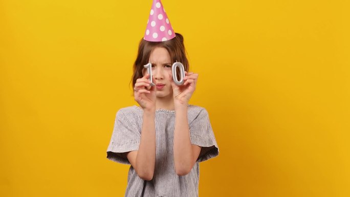 快乐，积极的十岁生日女孩戴着派对帽，点着蜡烛