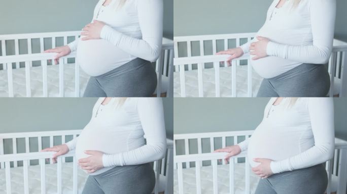 孕妇抚摸着自己的肚子，抚摸着婴儿床。等待孩子出生的准妈妈