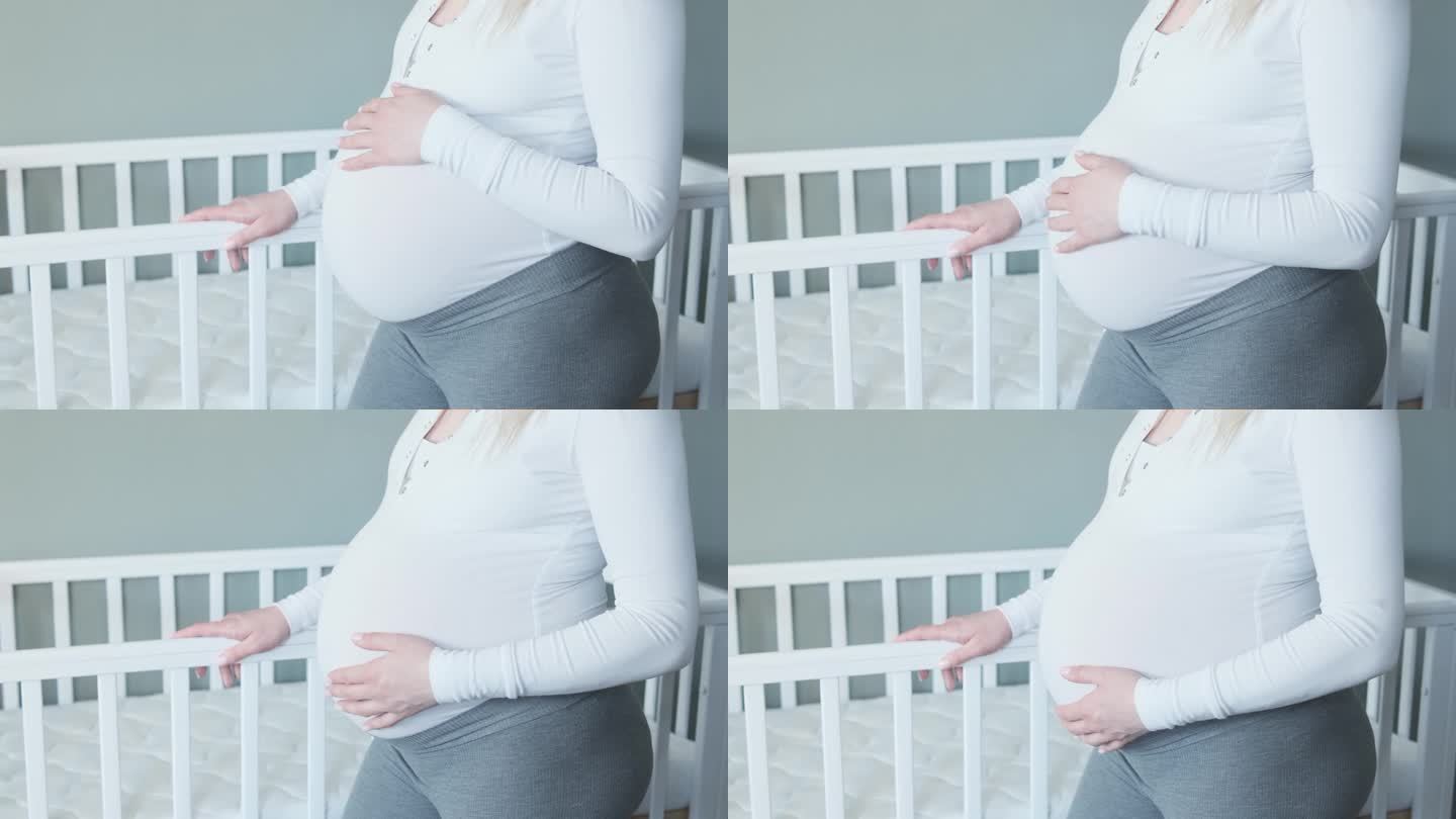 孕妇抚摸着自己的肚子，抚摸着婴儿床。等待孩子出生的准妈妈