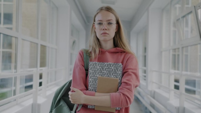 一个悲伤的年轻女子走在高中走廊上，手里拿着书，感觉很悲伤