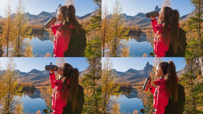 女徒步者喝水，欣赏秋天雄伟的山间湖景