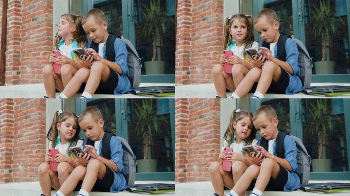 欢快时尚的小学生小男孩小女孩坐在户外楼梯上使用手机上网交流。友谊，科技理念。在线玩游戏。