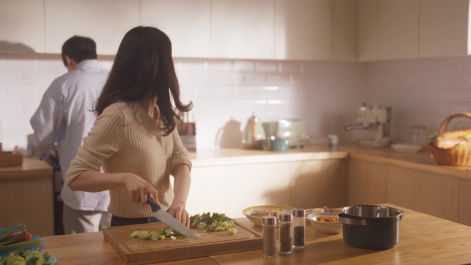 一对韩国年轻夫妇在家做饭的照片。相爱的男女朋友在厨房准备晚餐，一边做美味的食物一边进行有趣的交谈