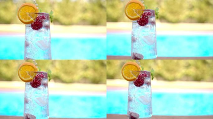 莫吉托鸡尾酒杯，加冰、樱桃、薄荷、苏打和杜松子酒，靠近蓝色泳池