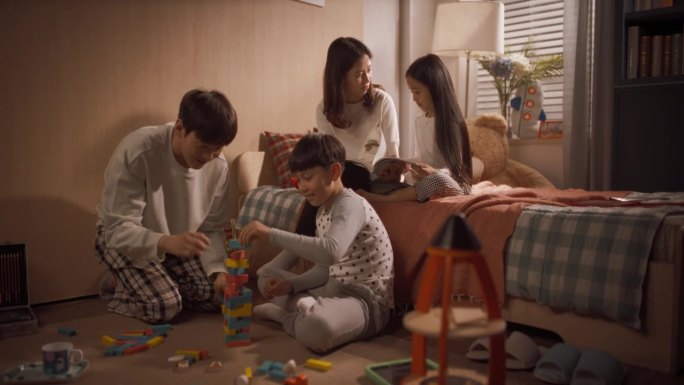 成功的韩国父母与孩子在儿童房玩耍。母亲和女儿读童话，父亲和儿子用积木搭一座塔。缩小多莉广角镜头