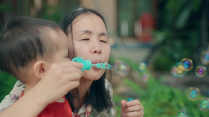 顽皮的亚洲男孩和妈妈在阳光公园享受泡泡游戏-家庭纽带和快乐时刻
