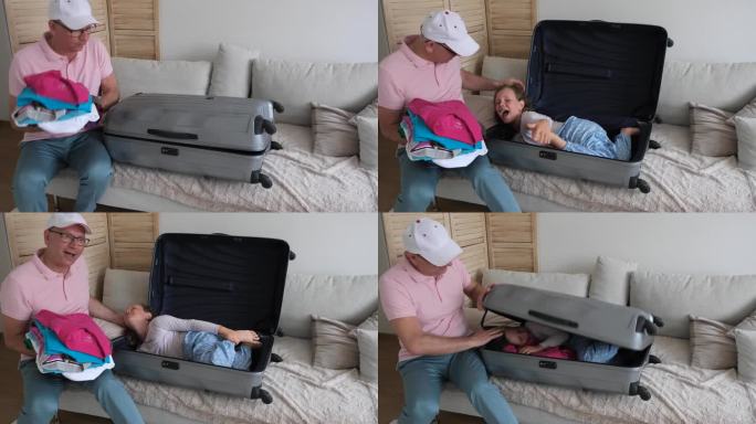 男人用手提箱打包东西。一个7-8岁的白人女孩从一个大行李箱里躲了出来，想要吓唬她的父亲。