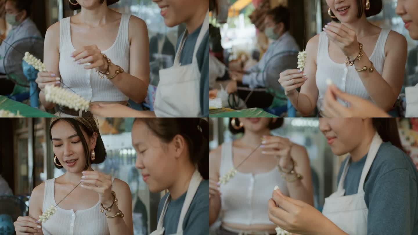 在曼谷花卉市场，一名亚洲女游客向泰国花店老板请教如何制作花环。