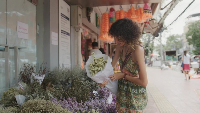 女游客在曼谷旅游时，在花市挑选鲜花。