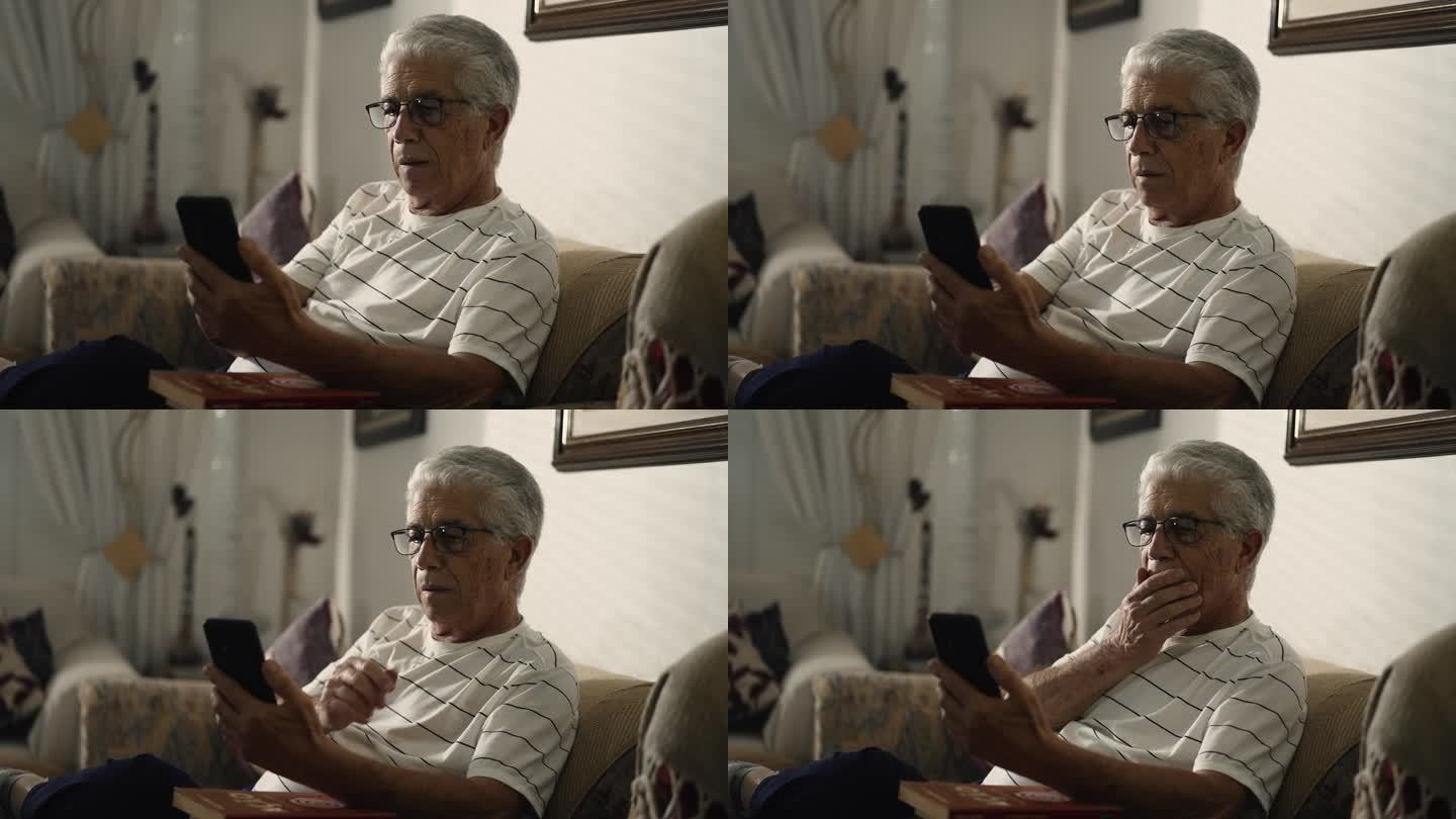老人坐在家里的沙发上盯着手机，一副忧心忡忡的样子，在网上看视频，满脸困惑
