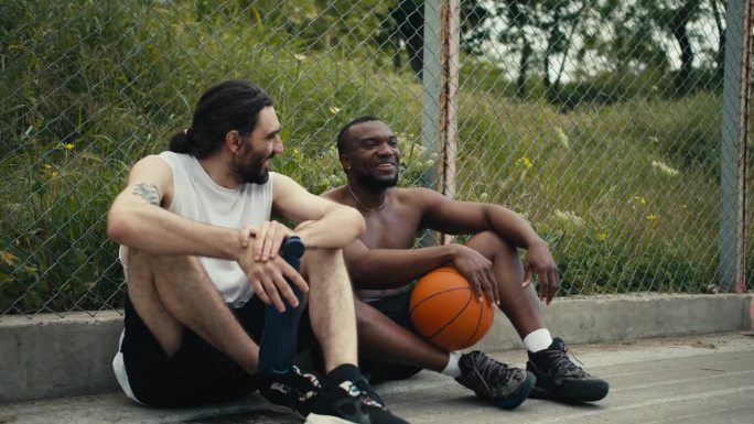 两个男人坐在篮球场的地板上，聊着正在进行的比赛，他们很高兴能参加比赛