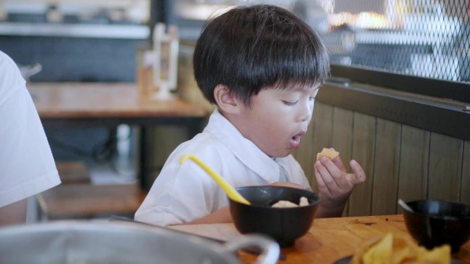 小亚洲男孩在涮餐厅吃饭前吹着热汤