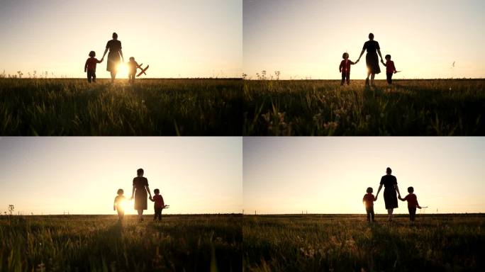 年轻家庭的剪影——母亲和两个兄弟双胞胎男孩一起走在户外或公园的阳光下，黄金时刻，闪耀着快乐的母亲和孩