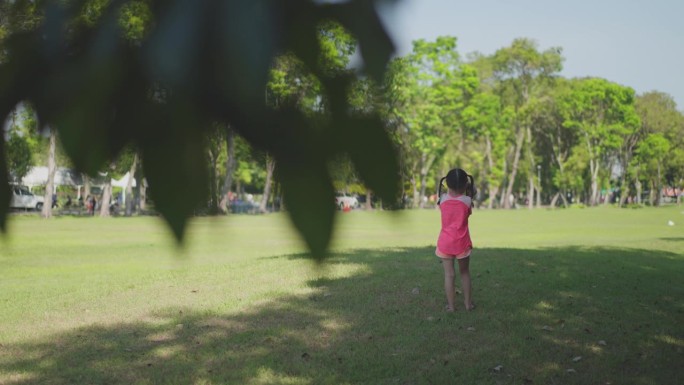6岁的小亚细亚在周末用双筒望远镜在花园里探索新鲜有趣的事物。扎着小辫子、穿着粉色连衣裙的女孩透过双筒
