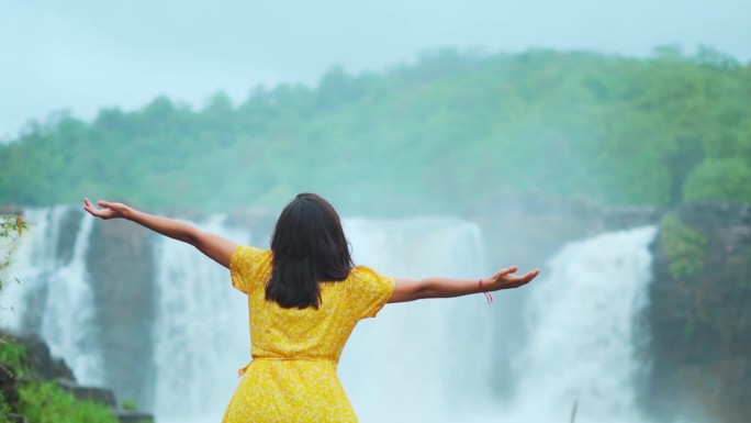旅游少女在印度古吉拉特邦美丽的吉拉瀑布前张开双臂。在旅游目的地享受假期的女性。雨季时瀑布流动。