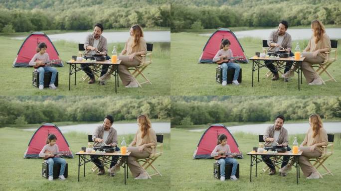 暑假周末，可爱的女儿在露营帐篷里唱歌和弹奏尤克里里琴，与父母在草地上放松，野餐。